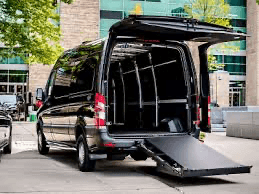 Black van with open rear doors and a folded ramp, parked near a building.