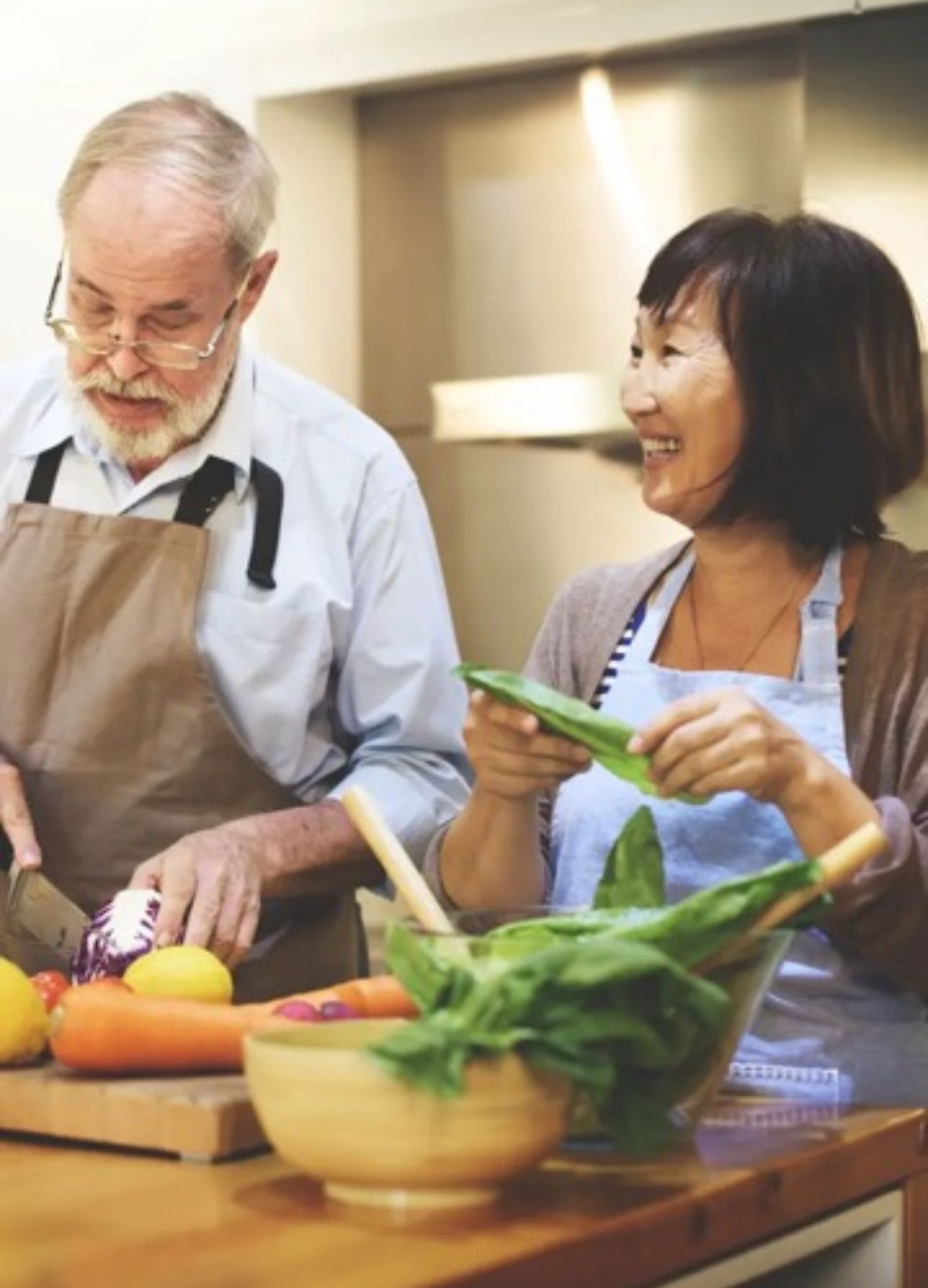 Two adults preparing vegetables on a kitchen counter, with various fresh ingredients and kitchen utensils visible.