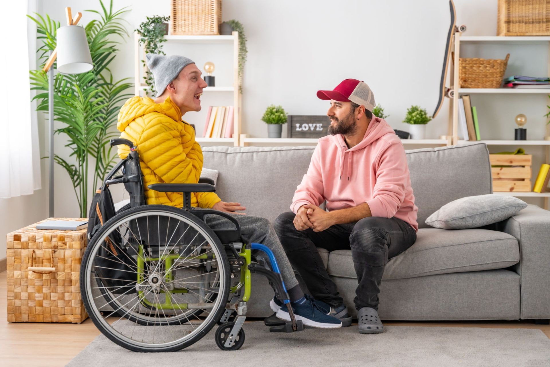 Two people happily chatting in a cozy living room, one sitting in a wheelchair.